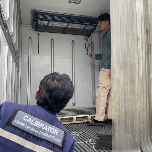 Technician in a teal shirt stands inside a metal cargo van, pointing at an overhead device while another worker watches from the foreground wearing a CALIBRATOR vest.]','Inside a transport lab van, a technician inspects equipment mounted on the ceiling as another worker looks on.